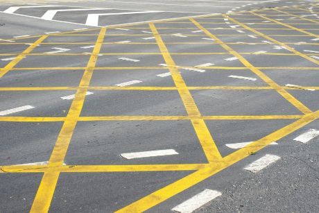 Yellow line painted hatched road markings on a concrete road that has white line painted road markings.