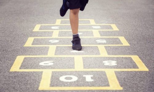 Yellow hops scotch line painting on a playground with a person wearing black shoes and shorts playing the hops scotch jumping number game.